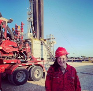 Women wearing a red hat and jacket standing in front of heavy machinery.