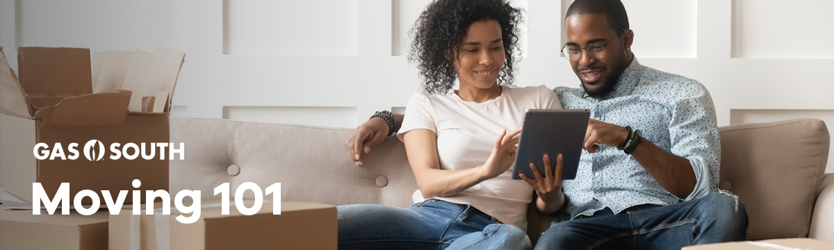 A couple sitting on the couch looking at an iPad with moving boxes around them.