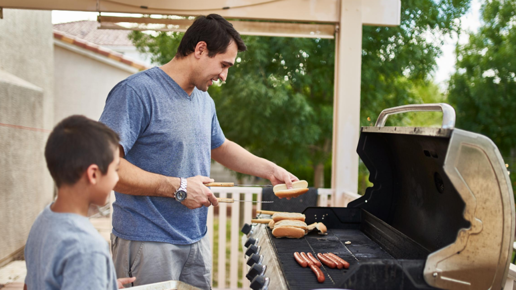 man cooking hot dogs on gas grill