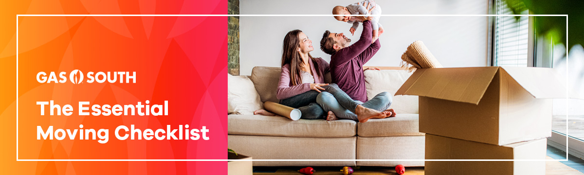 A woman and man sitting on the couch holding a child with moving boxes around them.